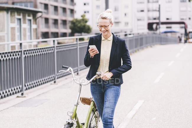 Блондинка пригородная колесница велосипед во время использования мобильного телефона на мосту — стоковое фото
