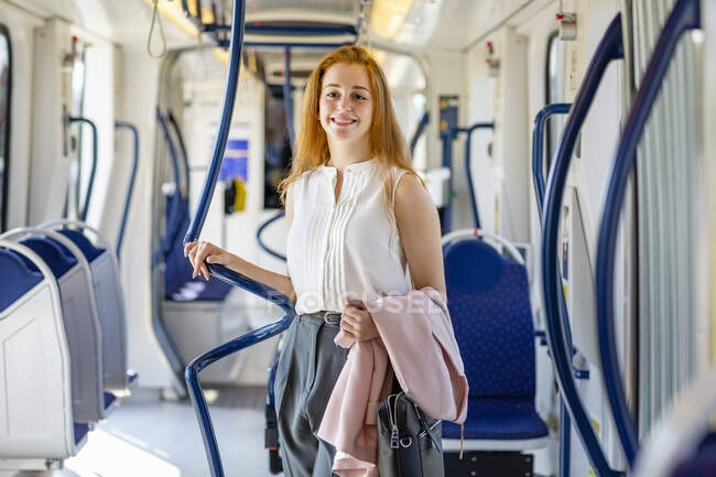 Sonriente joven empresaria llevando bolsa y chaqueta en tren - foto de stock