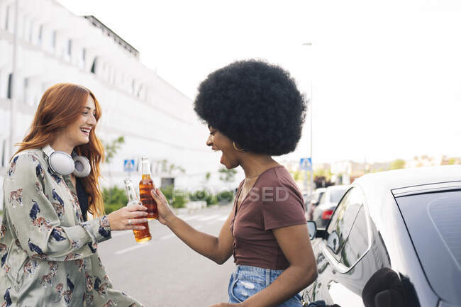 Allegro afro donna brindare bottiglie di birra con amica al bordo della strada — Foto stock