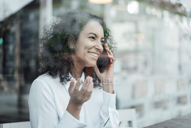 Joven mujer de negocios sonriendo mientras habla en el teléfono móvil sentado en la cafetería - foto de stock