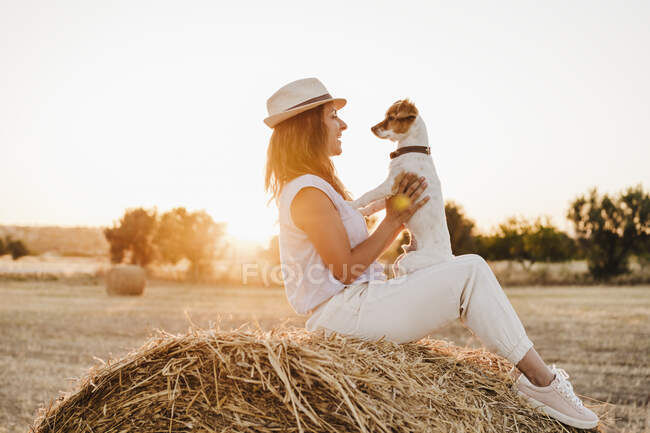 Frau mit Hut spielt mit Hund auf Strohballen — Stockfoto