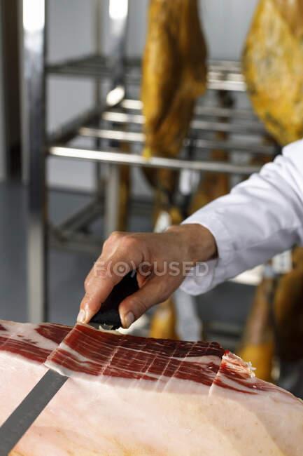 Мужчина-мясник режет ветчину в розничном магазине — стоковое фото