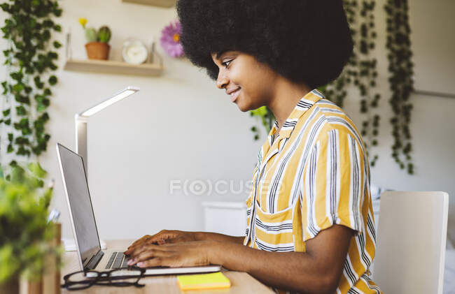 Усміхнена жінка використовує ноутбук, сидячи вдома — стокове фото