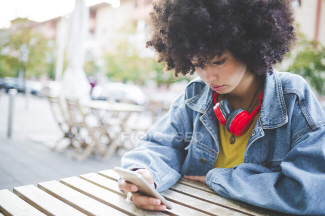 Giovane donna con acconciatura afro utilizzando lo smartphone in un caffè all'aperto in città — Foto stock