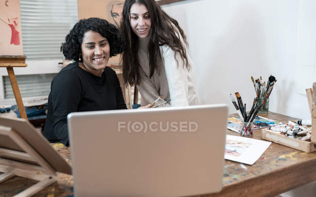 Посмішка молодих жінок-художників на відео-дзвінках через лептоп в художній студії — стокове фото