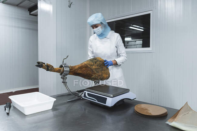 Woman measuring weight of ham leg on scale in factory — Stock Photo