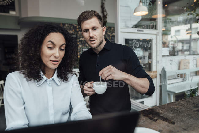 Geschäftsmann kocht Kaffee, während er mit Kollegen am Laptop im Café arbeitet — Stockfoto