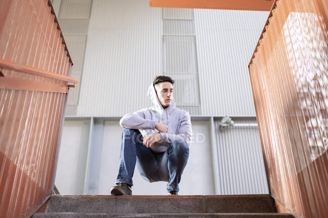 Bonito jovem olhando para longe enquanto se agacha na escadaria — Fotografia de Stock