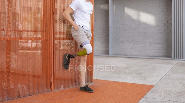 Jeune homme amputé debout avec les mains dans les poches contre le mur métallique orange — Photo de stock