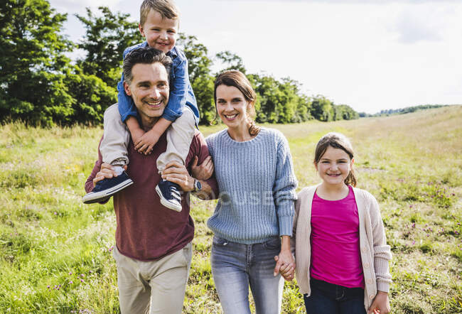 Famiglia sorridente che cammina sul prato nella giornata di sole — Foto stock