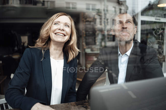 Smiling blond senior businesswoman sitting with male colleague in cafe seen through glass window — Stock Photo