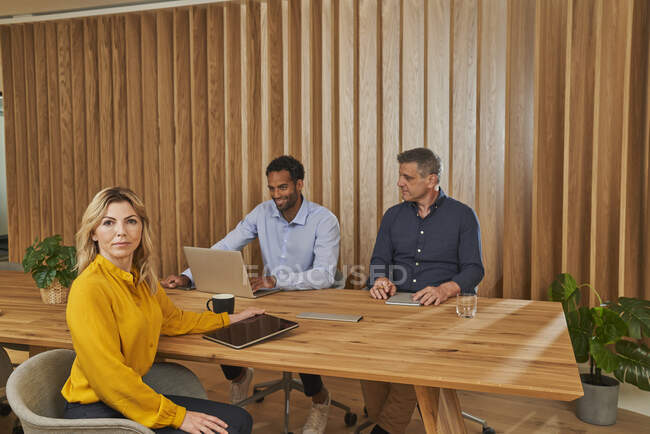 Empresária sentada com colegas do sexo masculino na mesa de conferência na sala de bordo — Fotografia de Stock
