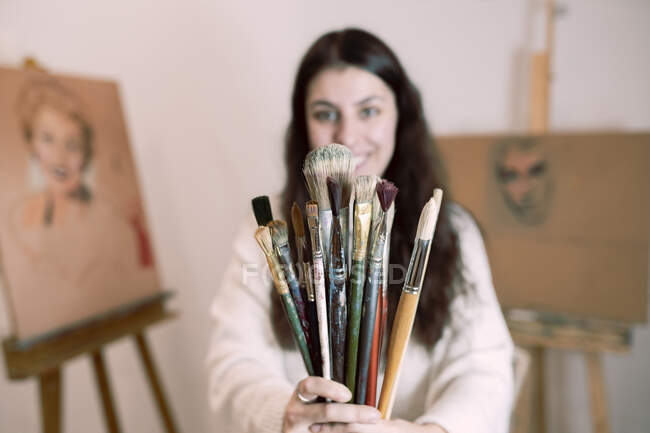 Young female painter holding variety of paintbrushes at studio — Stock Photo