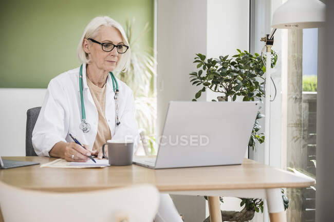 Female doctor writing while working at desk — Stock Photo