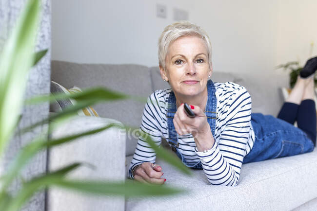 Woman holding remote control while lying on sofa at home — Stock Photo