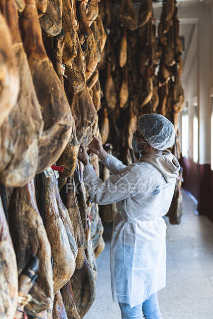 Worker with protective workwear looking at ham in slaughterhouse — Stock Photo