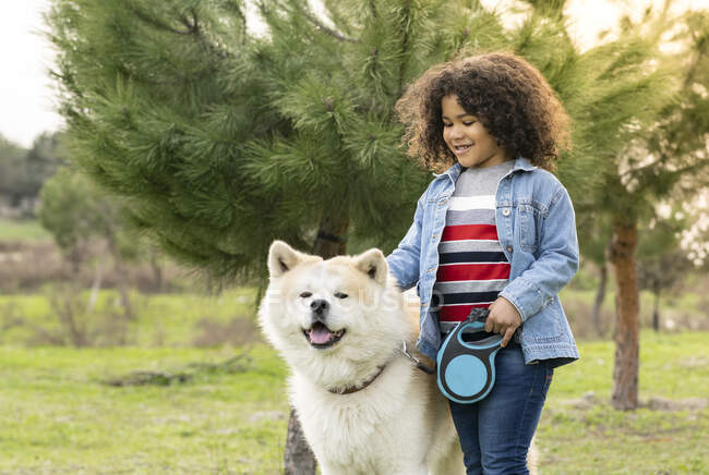 Smiling curly haired boy enjoying with dog in nature — Stock Photo