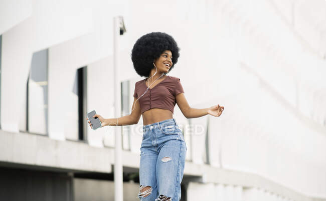 Mujer afro feliz mirando hacia otro lado mientras baila en la ciudad - foto de stock