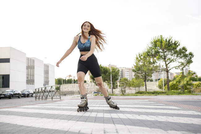 Smiling young redhead woman skating on road in city — Stock Photo