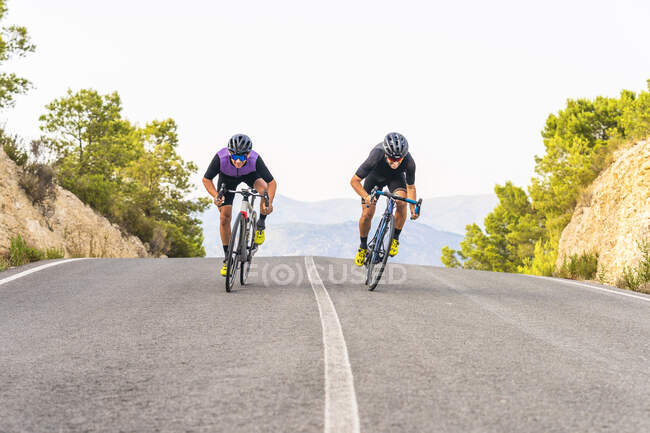 Sportivi maschi che cavalcano biciclette su strada — Foto stock