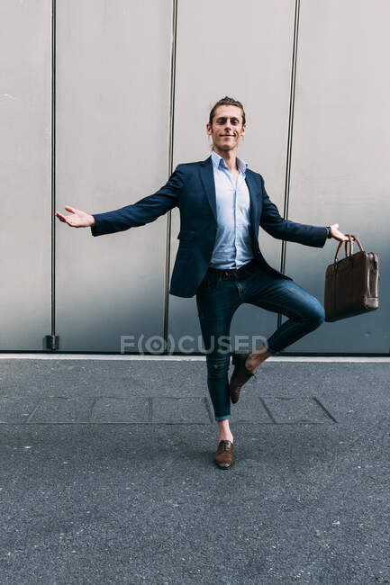Uomo d'affari sorridente con le braccia distese in piedi su una gamba davanti al muro — Foto stock