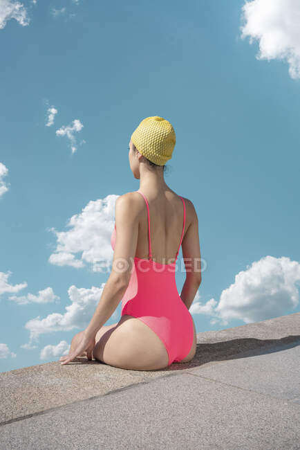 Woman with swimming cap and swimsuit sitting at edge — Stock Photo