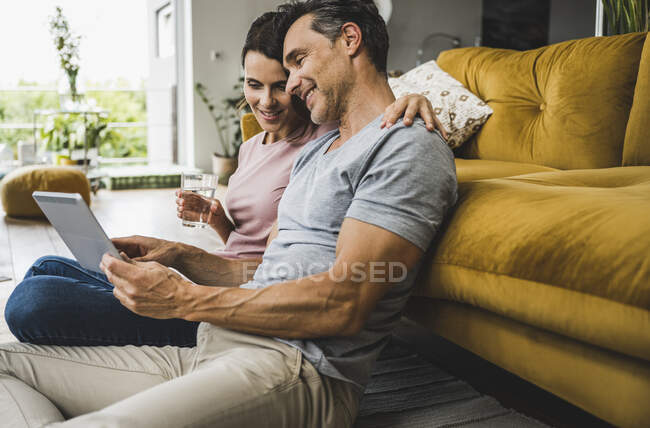 Femme tenant verre d'eau tandis que l'homme utilisant la tablette numérique à la maison — Photo de stock