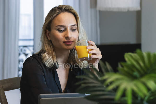 Empresaria sosteniendo vaso de jugo mientras mira la tableta digital en casa - foto de stock