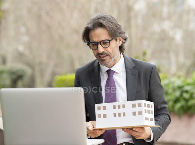 Male architect holding architectural model during video call through laptop — Stock Photo
