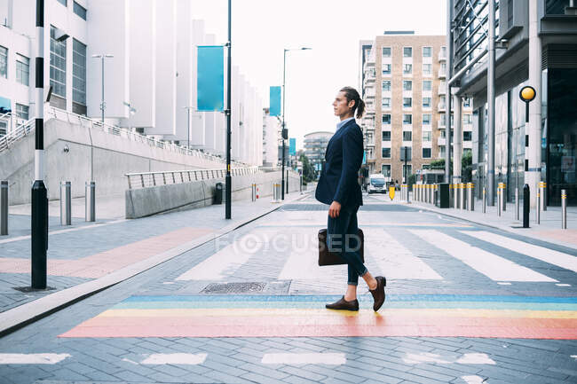 Businessman holding briefcase while walking on multi colored road markings in city — Stock Photo