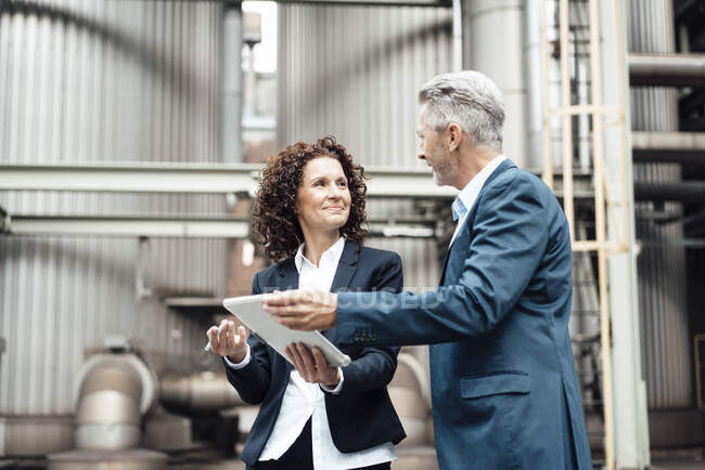 Businesswoman using digital tablet while discussing with colleague in front of industrial building — Stock Photo