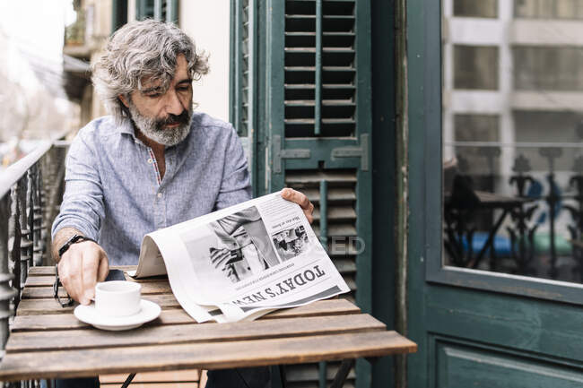 Man having coffee reading newspaper while sitting at table in balcony at house — Stock Photo