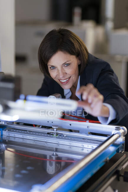 Smiling businesswoman examining machinery at illuminated factory — Stock Photo