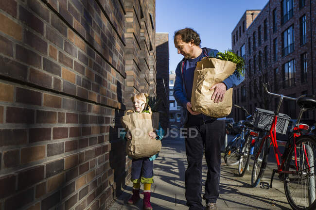 Uomo con figlia che tiene un sacchetto di carta di verdure mentre cammina sul vicolo — Foto stock