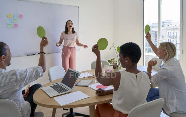 Cheerful businesswoman looking at coworkers holding paper for voting in meeting — Stock Photo