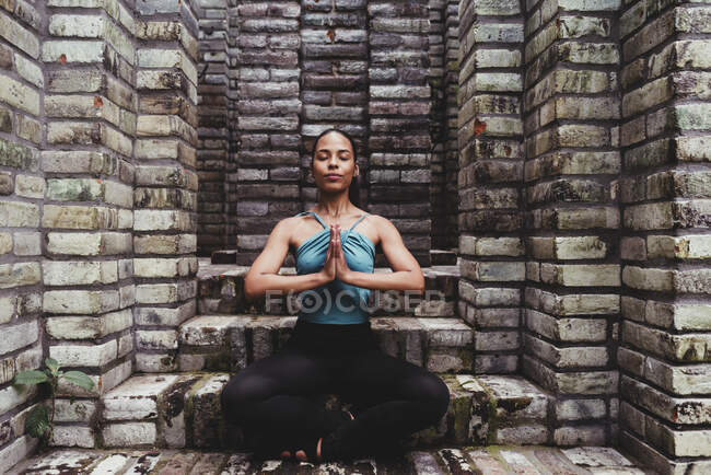 Young woman meditating with hands clasped in stone structure — Stock Photo