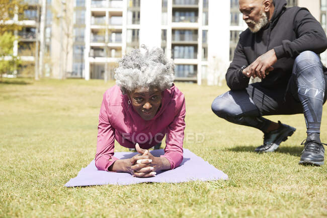 Man crouching near senior woman practicing plank position on exercise mat — Stock Photo
