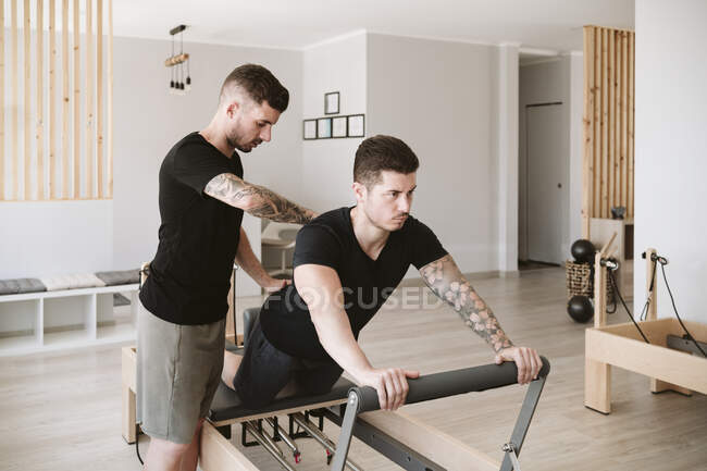 Male fitness trainer providing support while man practicing pilates in studio — Stock Photo