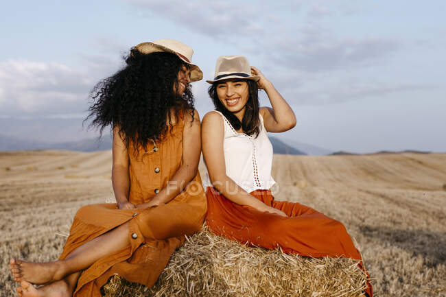 Femmes souriantes avec chapeau assis au champ — Photo de stock
