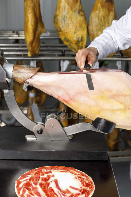 Carnicero macho rebanando pierna de jamón ibérico en tienda - foto de stock