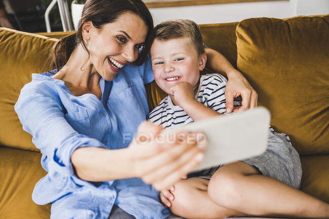 Frau macht Selfie mit Sohn per Smartphone auf Sofa zu Hause — Stockfoto
