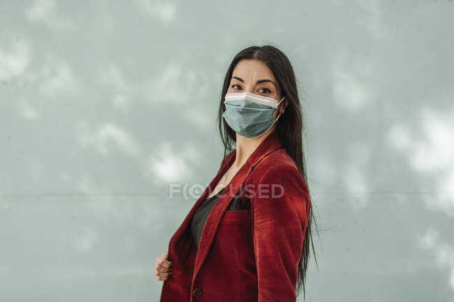 Geschäftsfrau im roten Blazer trägt bei Pandemie Schutzmaske gegen türkisfarbene Wand — Stockfoto
