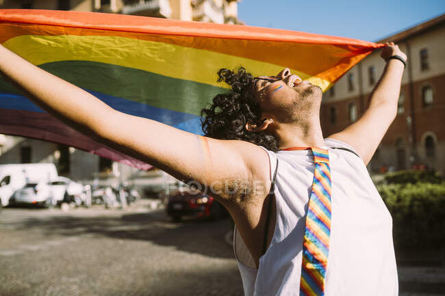 Young male activist looking up while holding rainbow flag on street — Stock Photo