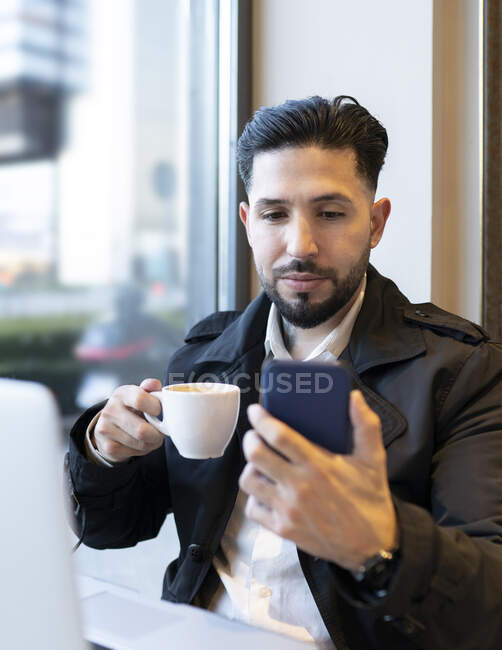 Чоловік-підприємець тримає чашку кави під час відеодзвінка в кафе — стокове фото