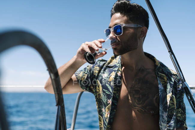 Молодой человек смотрит в сторону, выпивая на яхте во время отпуска — стоковое фото
