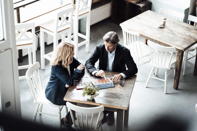 Зрелый бизнесмен обсуждает за цифровым планшетом с коллегой-женщиной, сидящей за столом в кафе — стоковое фото