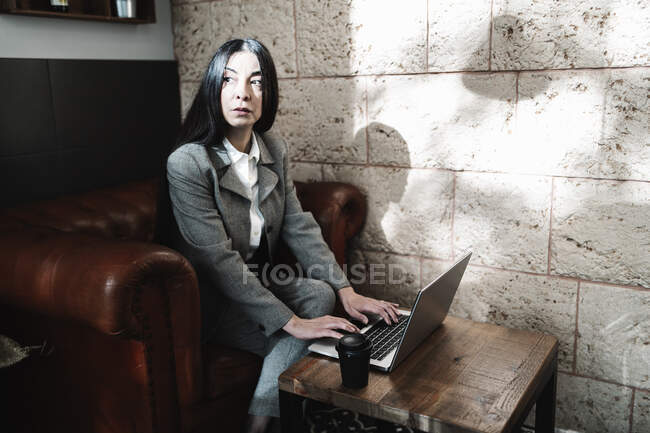 Serious businesswoman working on laptop looking away while sitting in cafe — Stock Photo