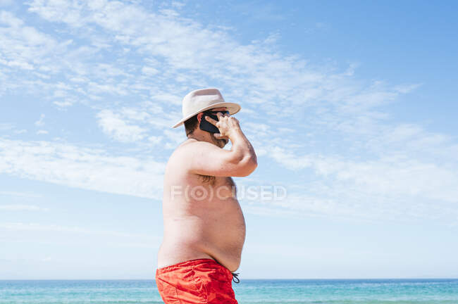 Mature homme en surpoids parlant sur le téléphone intelligent à la plage pendant les vacances — Photo de stock