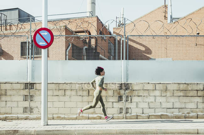 Femme en vêtements de sport courir sur le sentier par mur de briques — Photo de stock