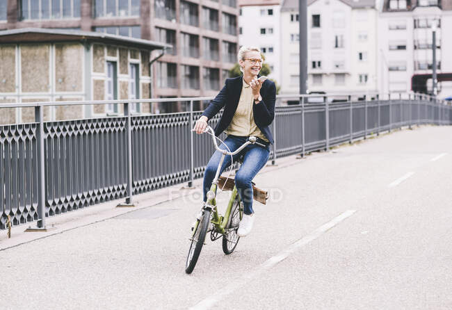 Счастливая пригородная женщина разговаривает по мобильному телефону во время езды на велосипеде по мосту — стоковое фото